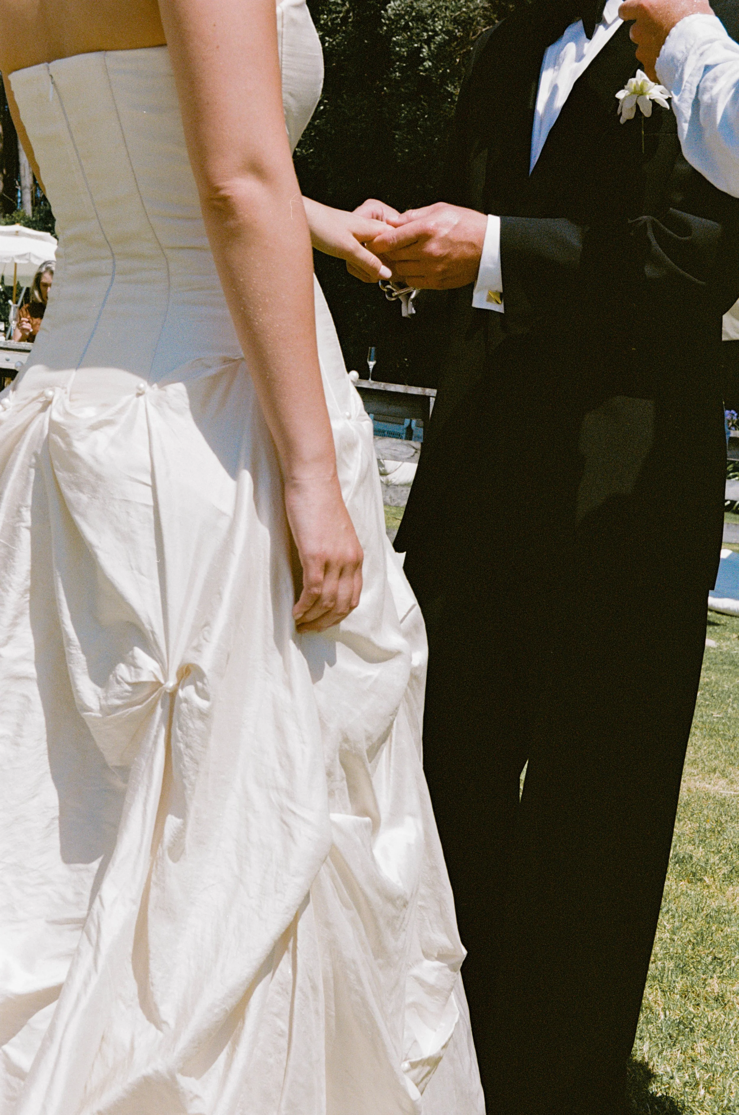 A bride and groom exchanging vows, with the groom holding the bride's hands, outdoors during a wedding ceremony.