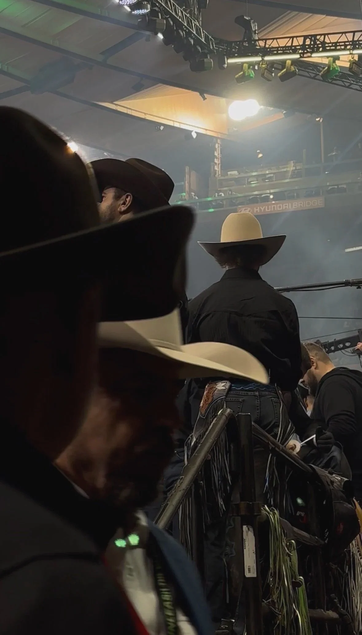 People wearing cowboy hats at an indoor event with stage lighting and equipment.