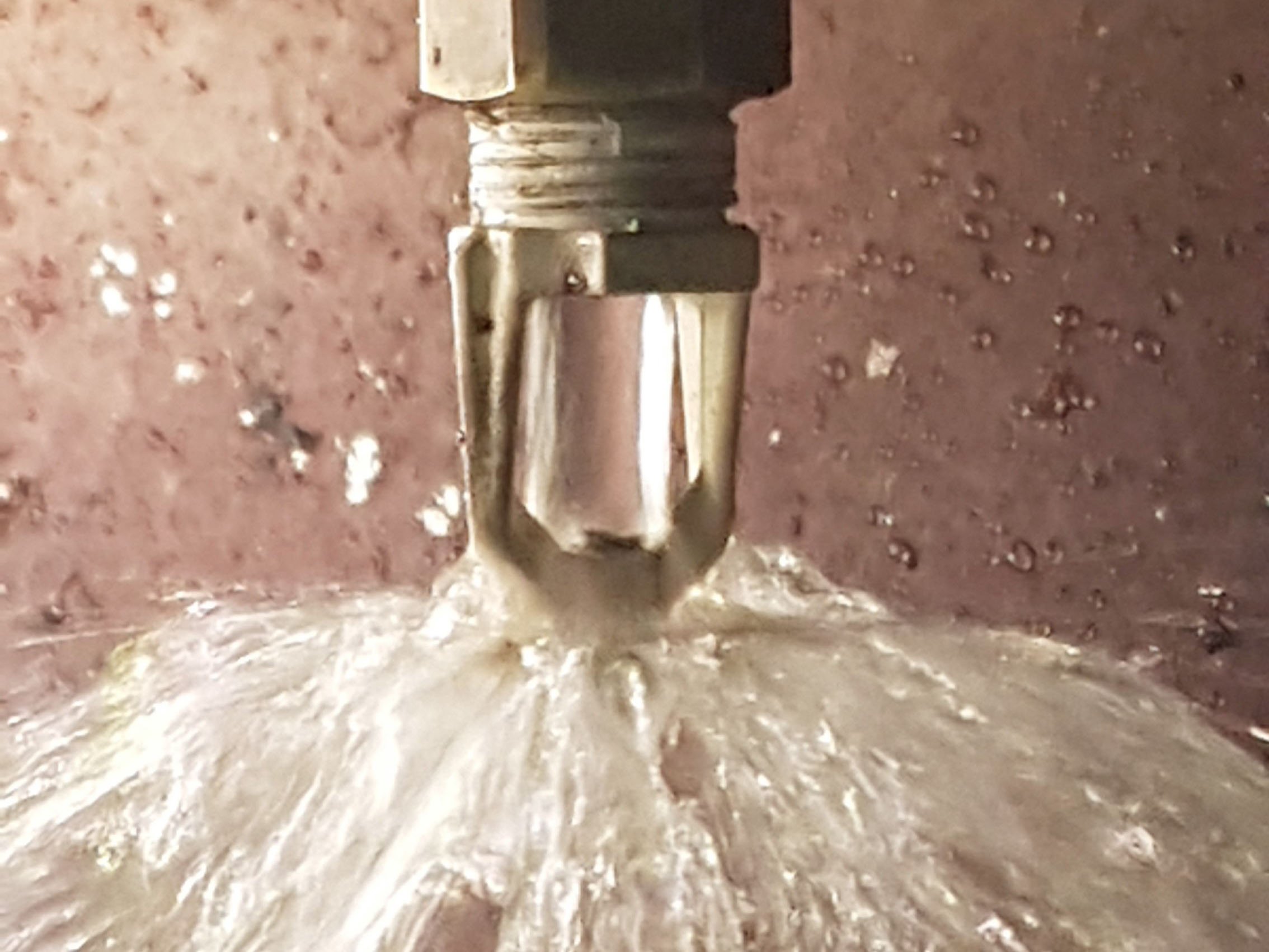 Close-up of a metallic pipe with water flowing out onto a reddish-brown surface.
