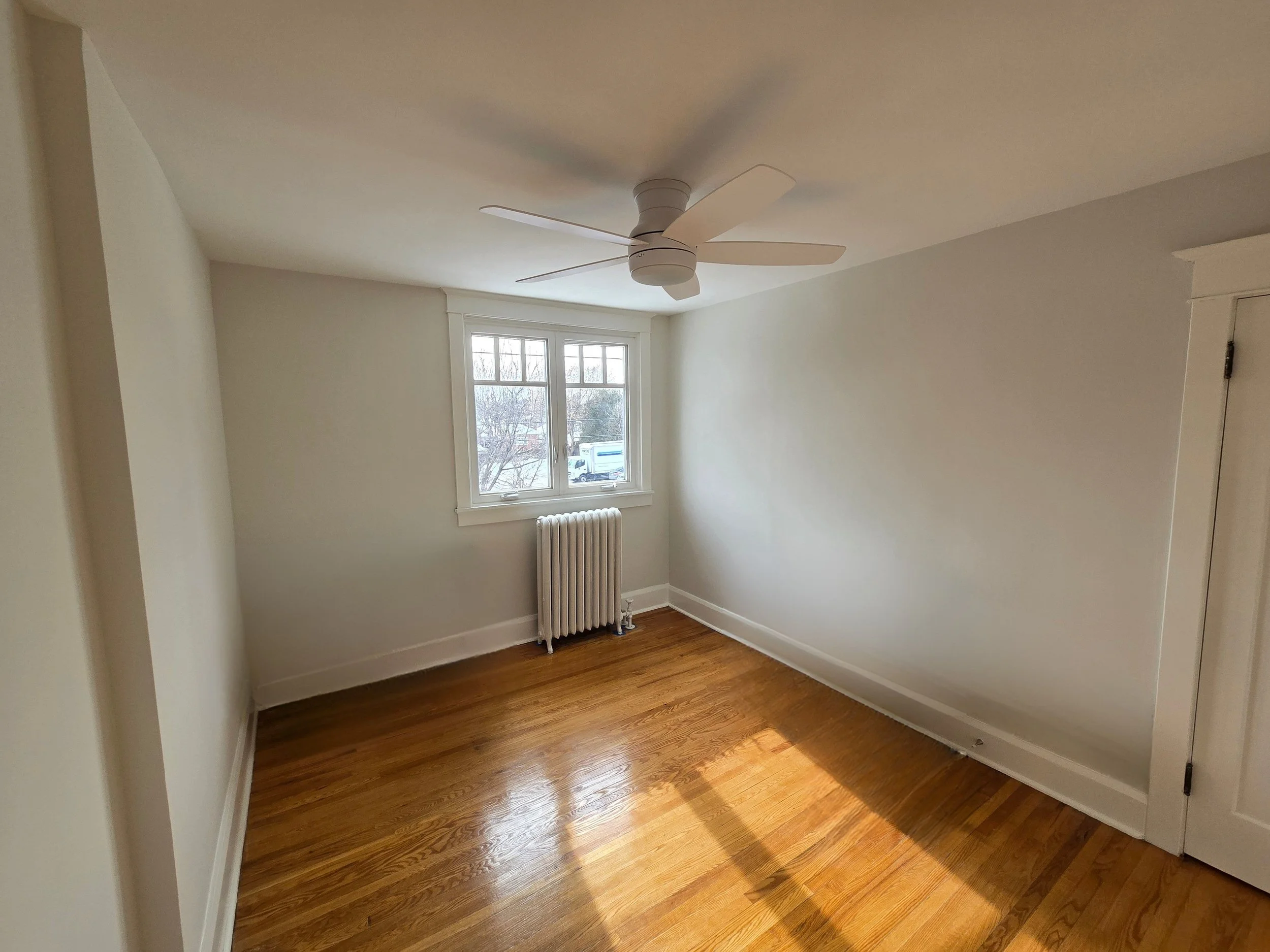 Empty room with hardwood floors, white walls, a window, and a white ceiling fan.