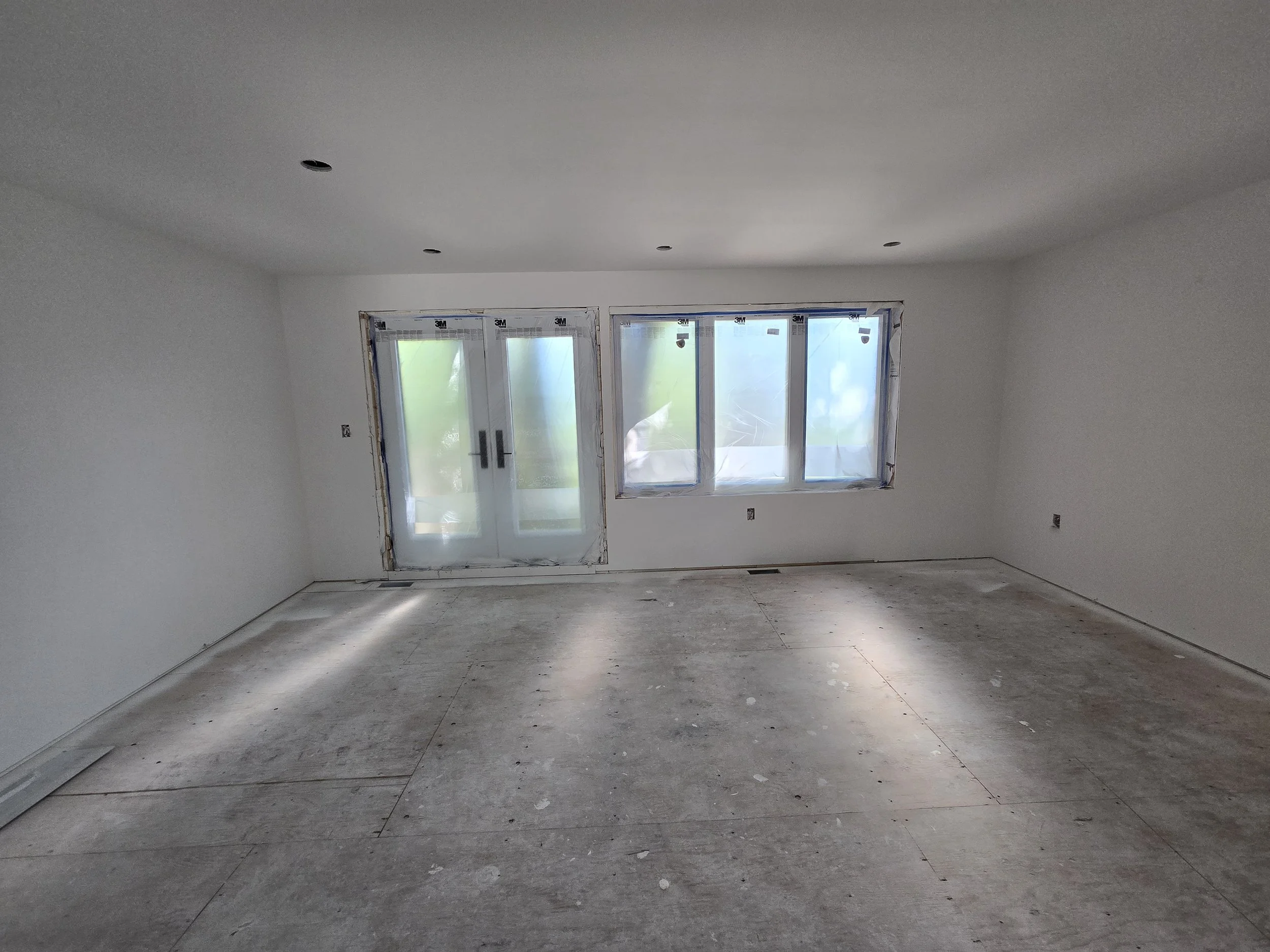 Empty room with partially installed windows and unfinished flooring.