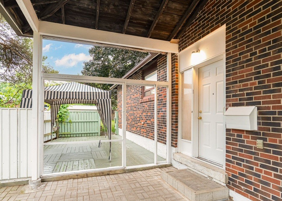 Back porch area with a screened-in section, a white door, and a swing under a striped canopy in the backyard. The yard has a green fence and some trees.