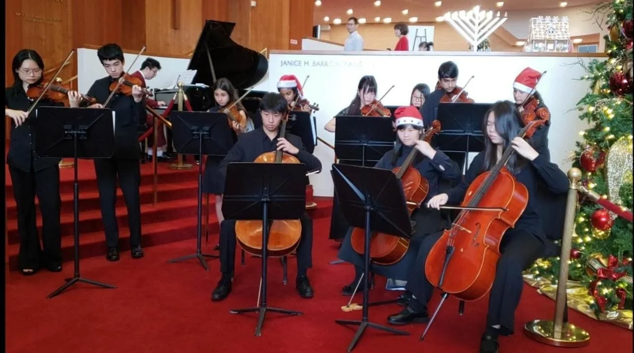 High school chamber orchestra performing in school gym wearing red and traditional attire