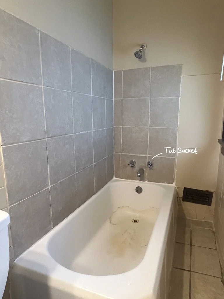 Empty bathroom bathtub with dirt marks, gray tiled wall, and labeled tub socket.