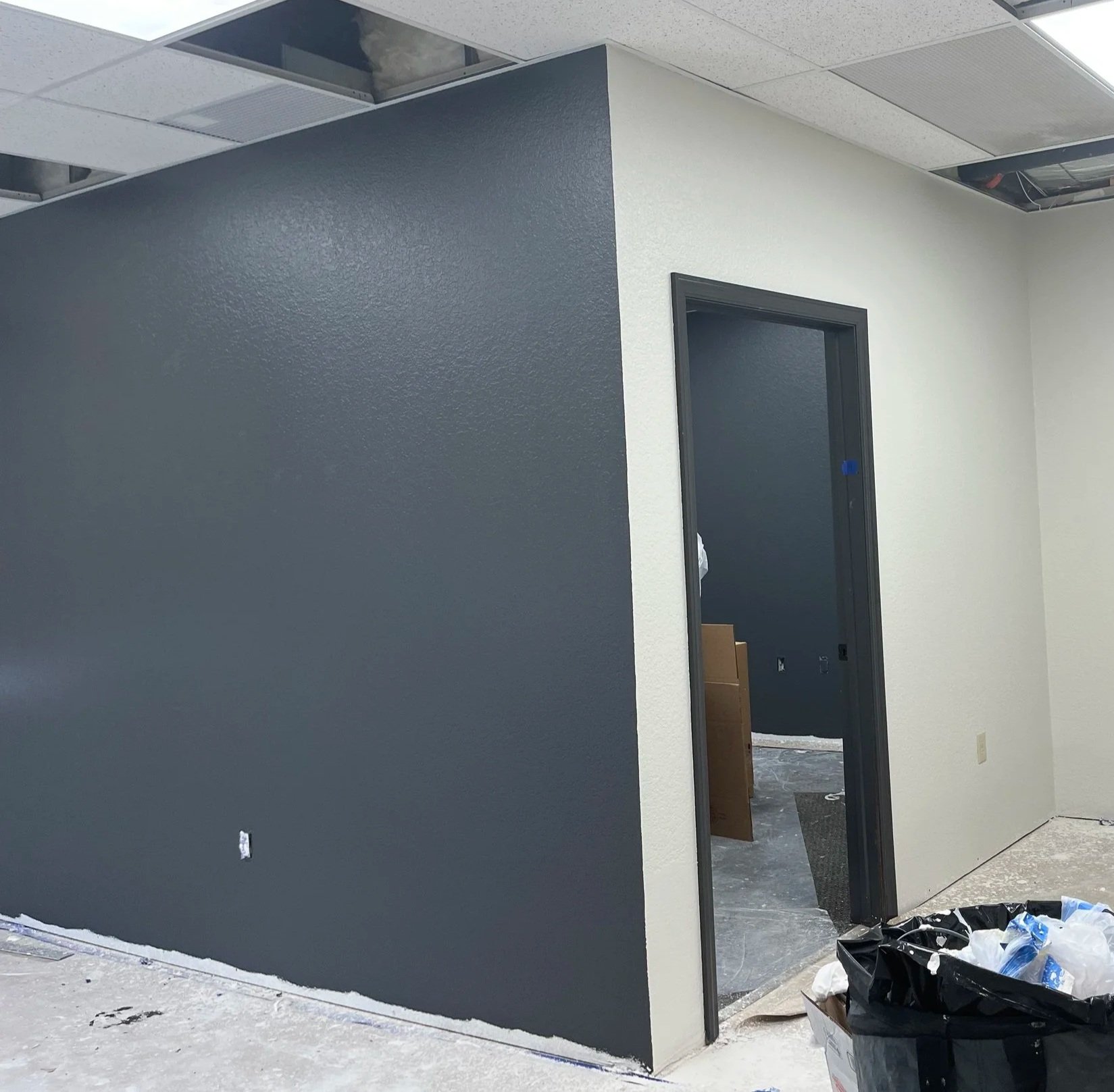 Interior of an office under construction with painted walls, open ceiling tiles, and construction materials on the floor.