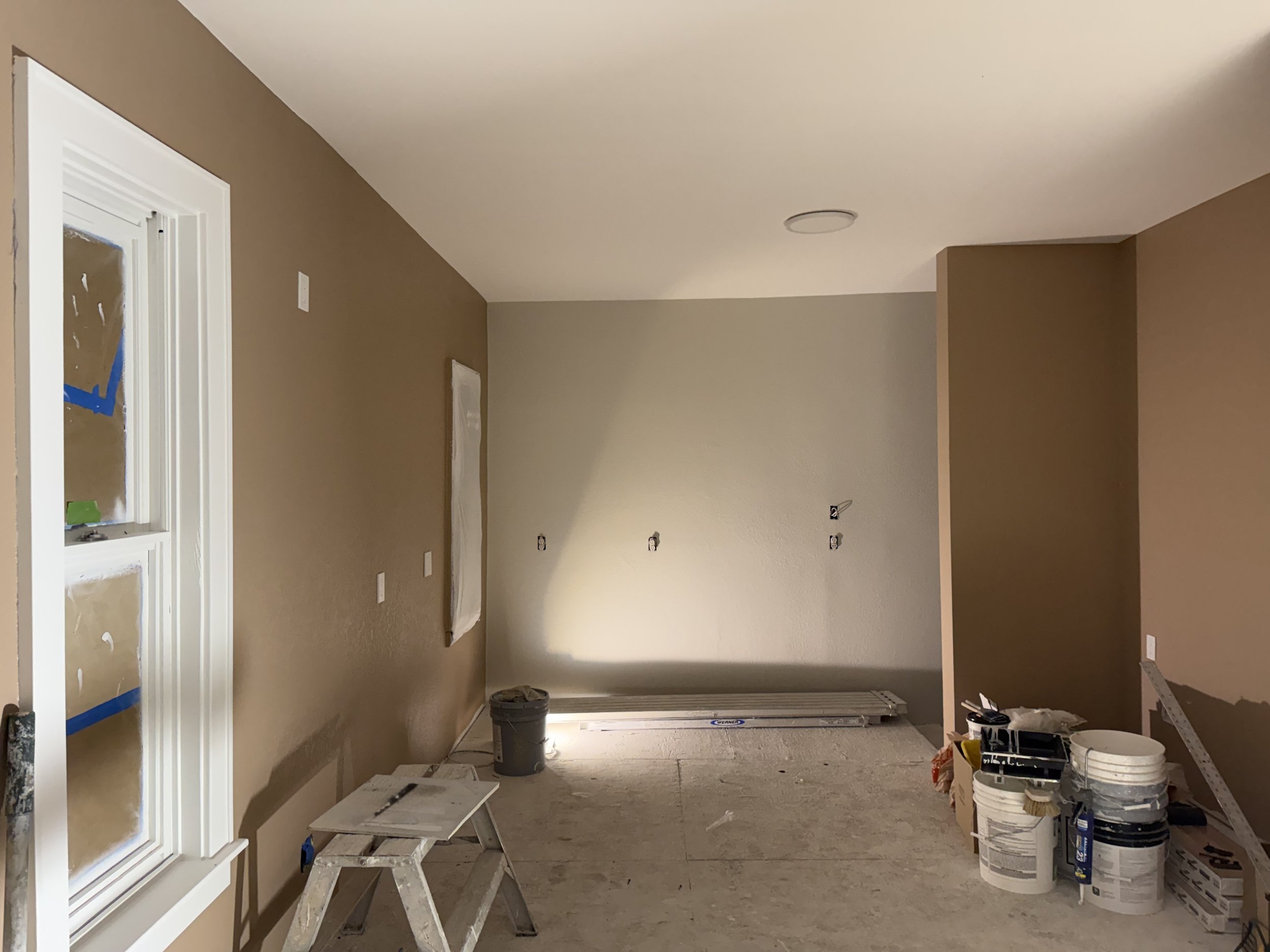 Room under renovation with construction materials, paint buckets, tools, and a step ladder.