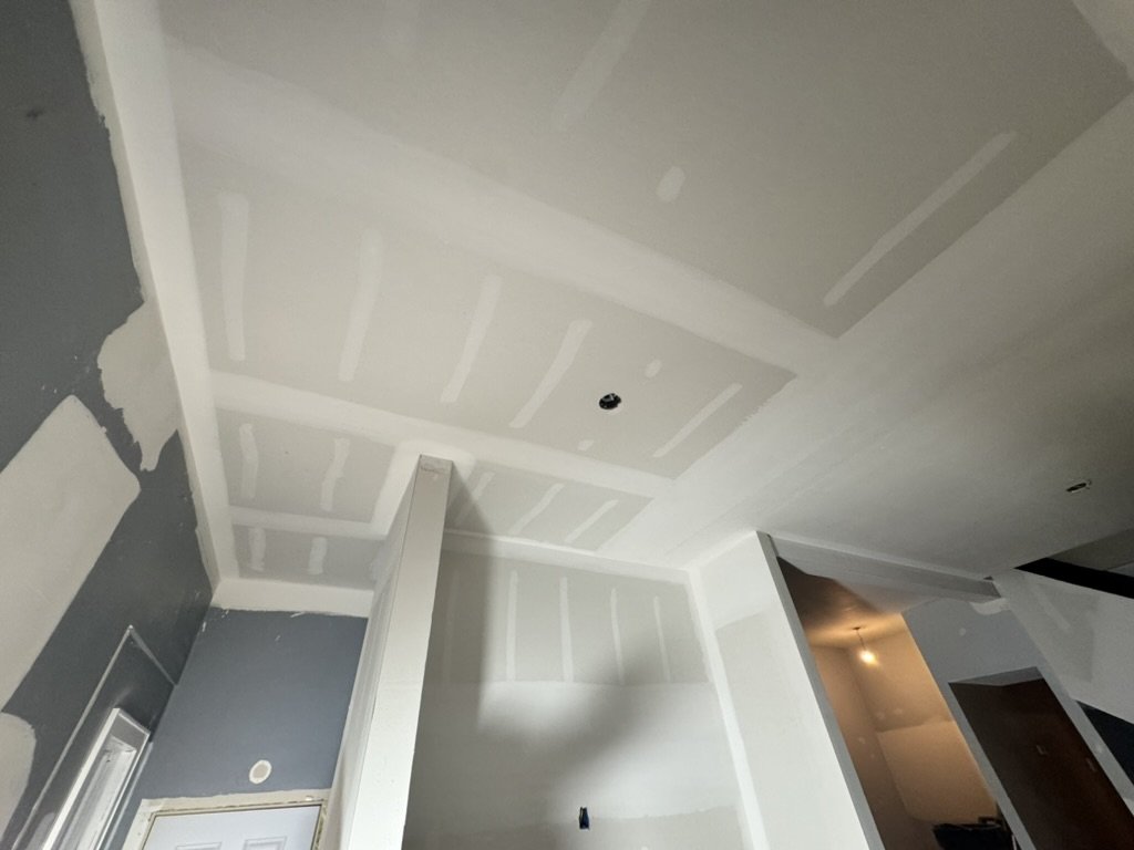 Interior construction with drywall installation, gray and white walls, ceiling with drywall seams, in a house under renovation.