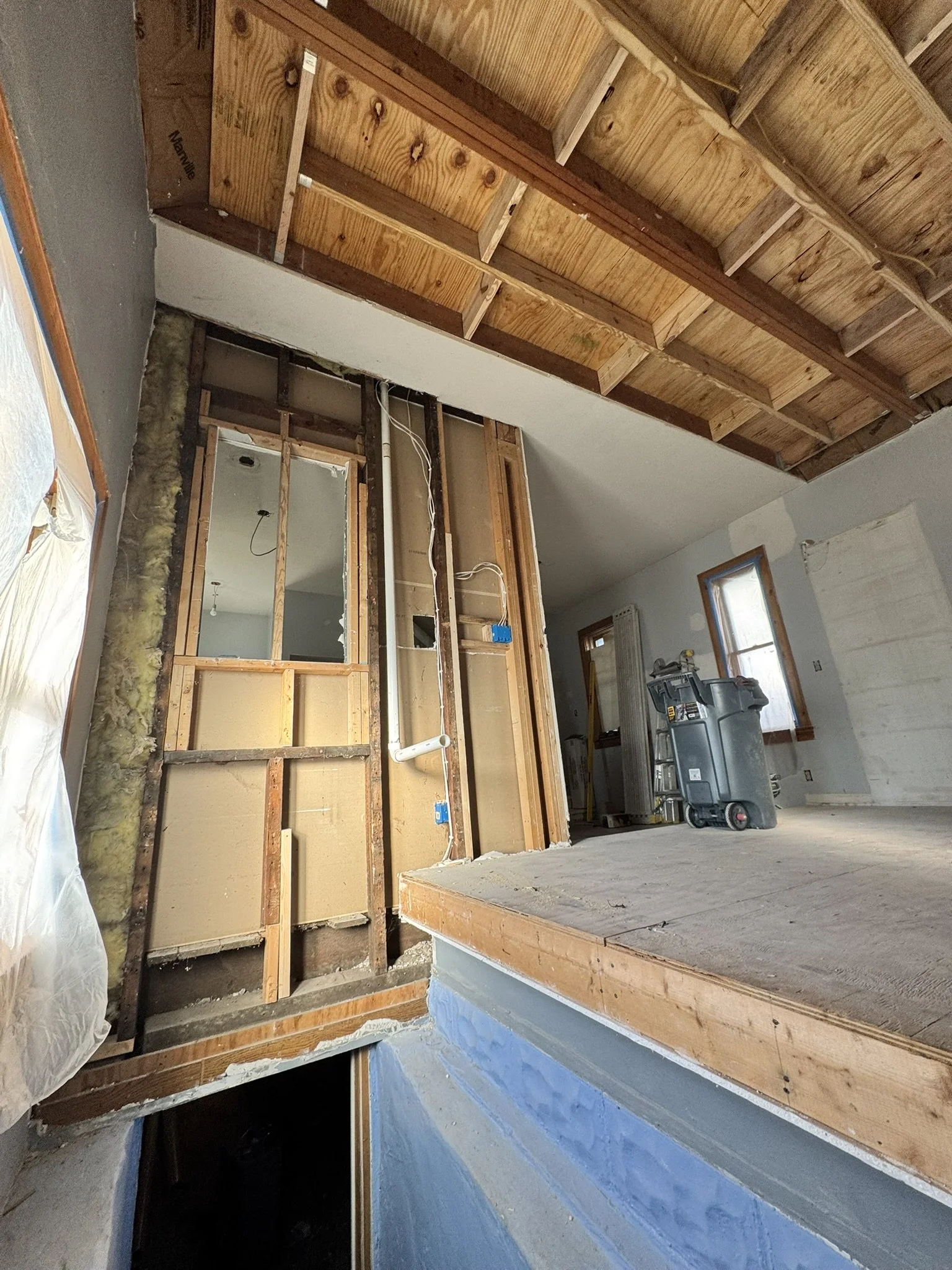 Interior of a house under renovation with exposed wooden framing and ceiling, construction tools, and partially removed walls.
