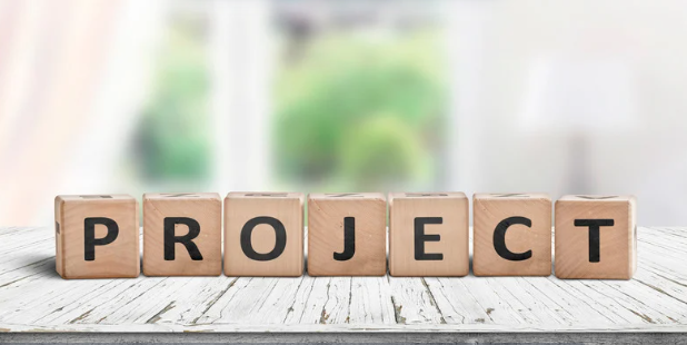 Wooden blocks spelling out the word 'PROJECT' on a white surface with a blurred background.