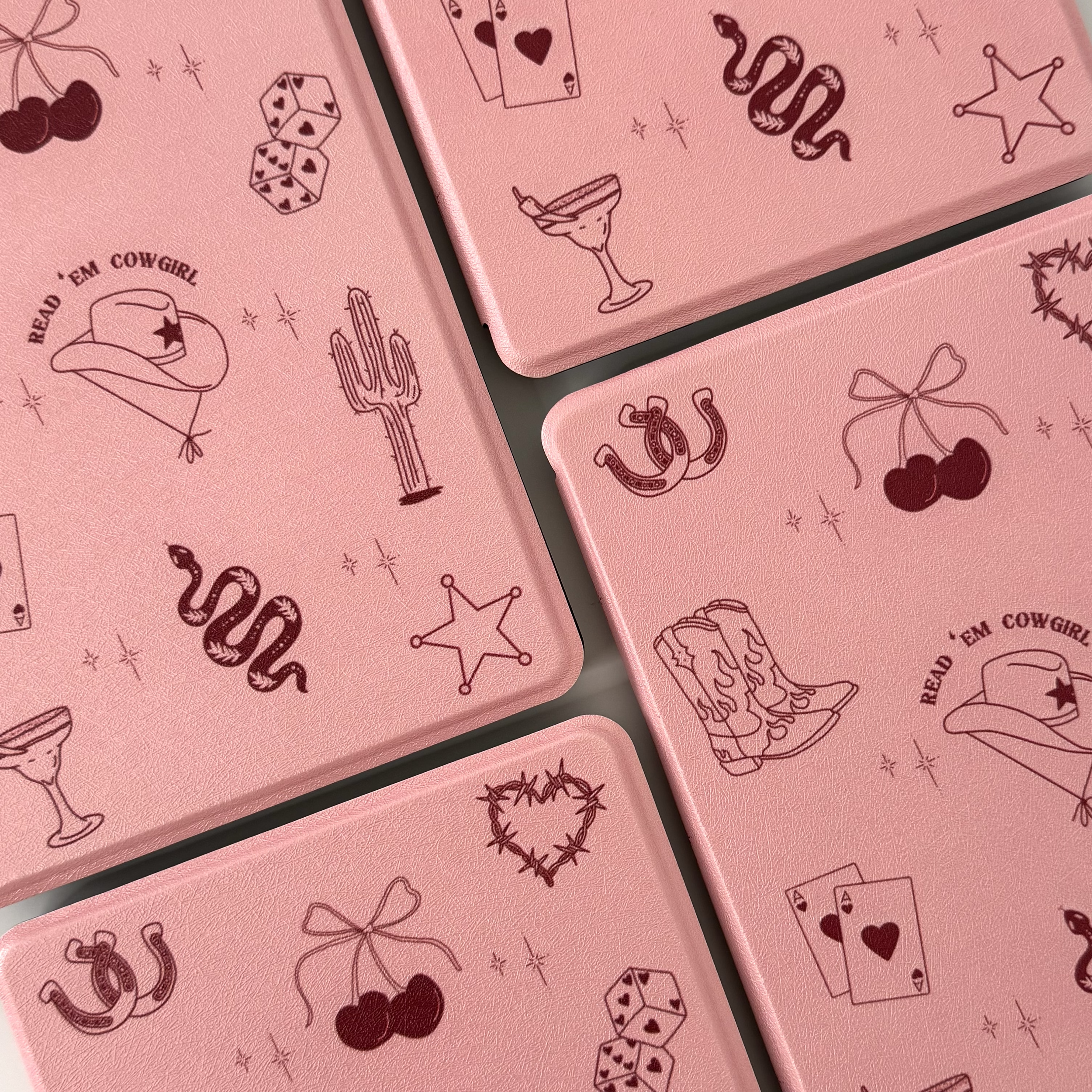 Close-up of pink metallic tins with cowgirl-themed illustrations including a cowboy hat with the phrase 'Read 'Em Cowgirl', a cactus, snake, cowboy boots, cherries, star, and dice.