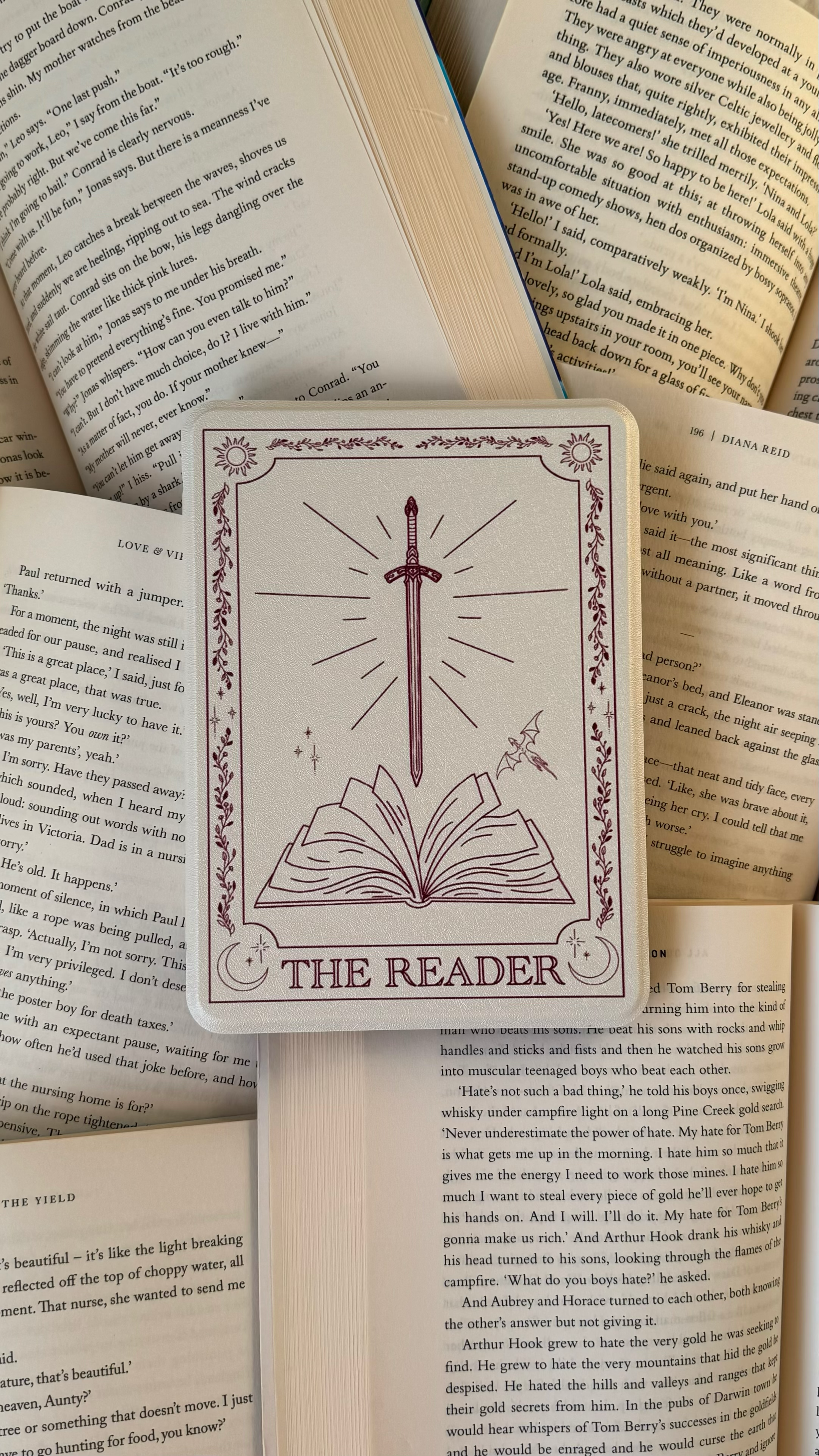 A card with a sword, open book, and celestial symbols, titled 'The Reader', placed on open books.