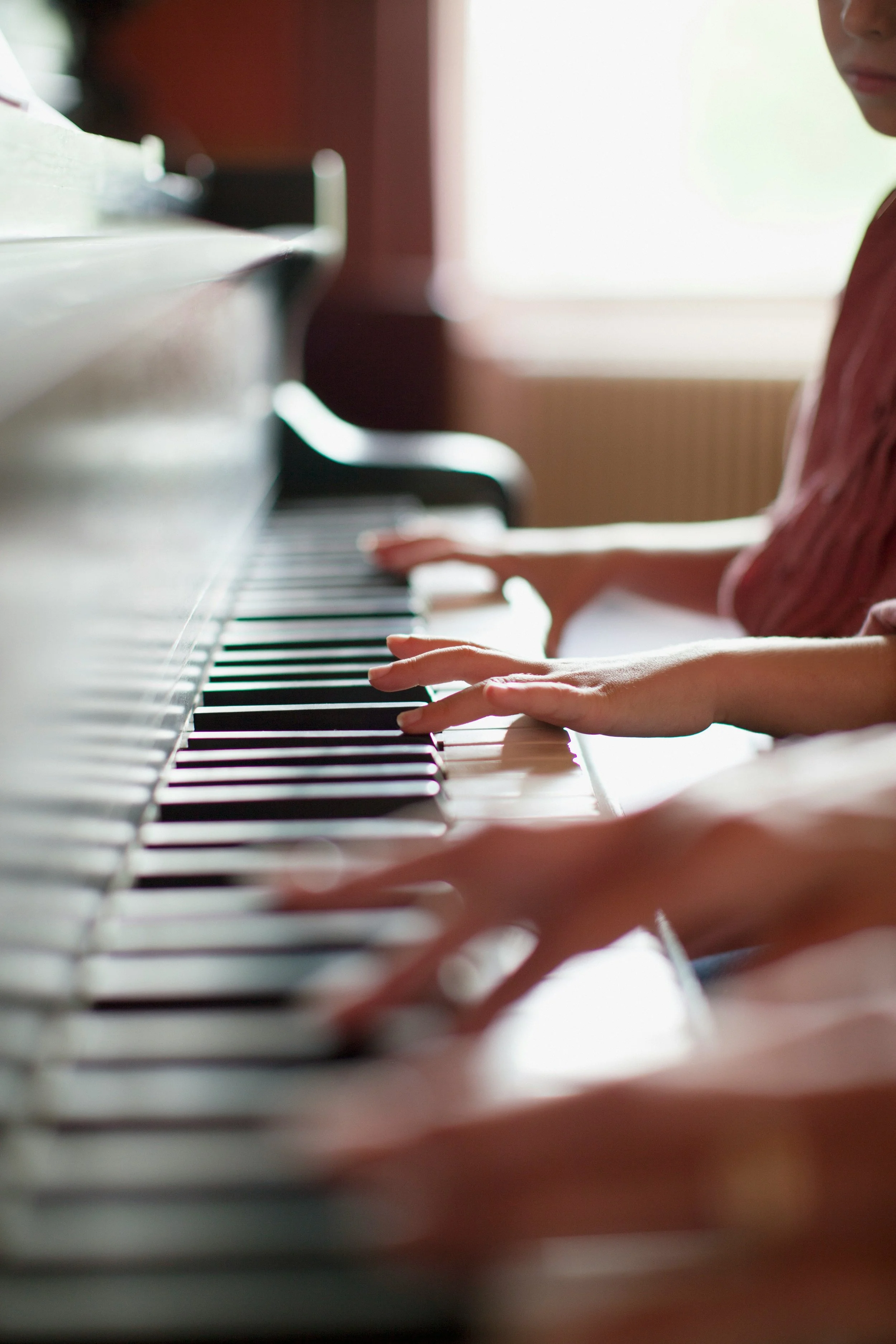 Two children playing piano together, focusing on their hands on the keys.