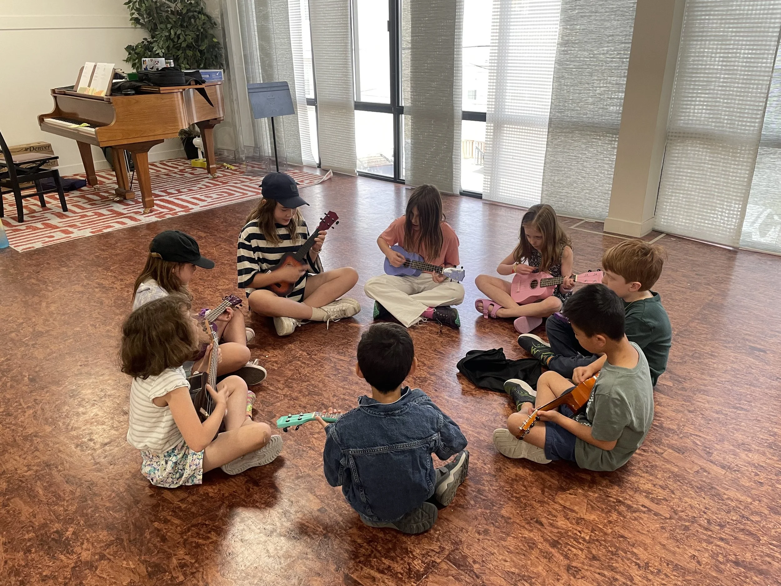 Group of children sitting in a circle in a music room, playing small guitars.
