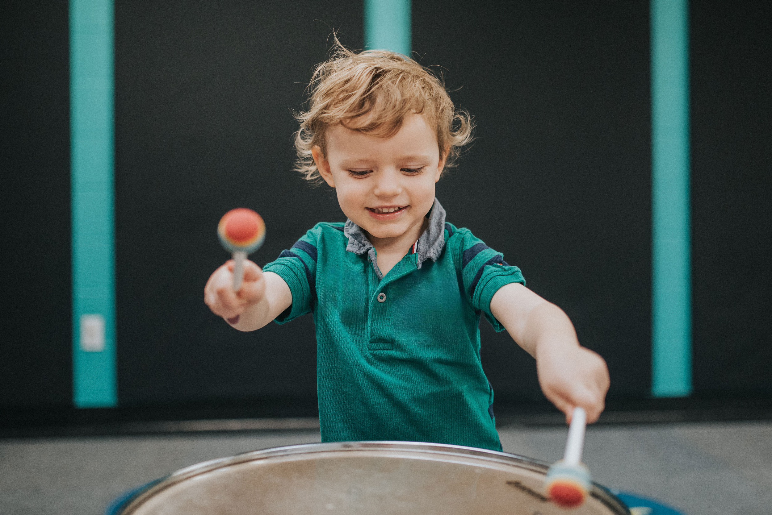 Young boy playing a floor drum with mallets, smiling, indoors.