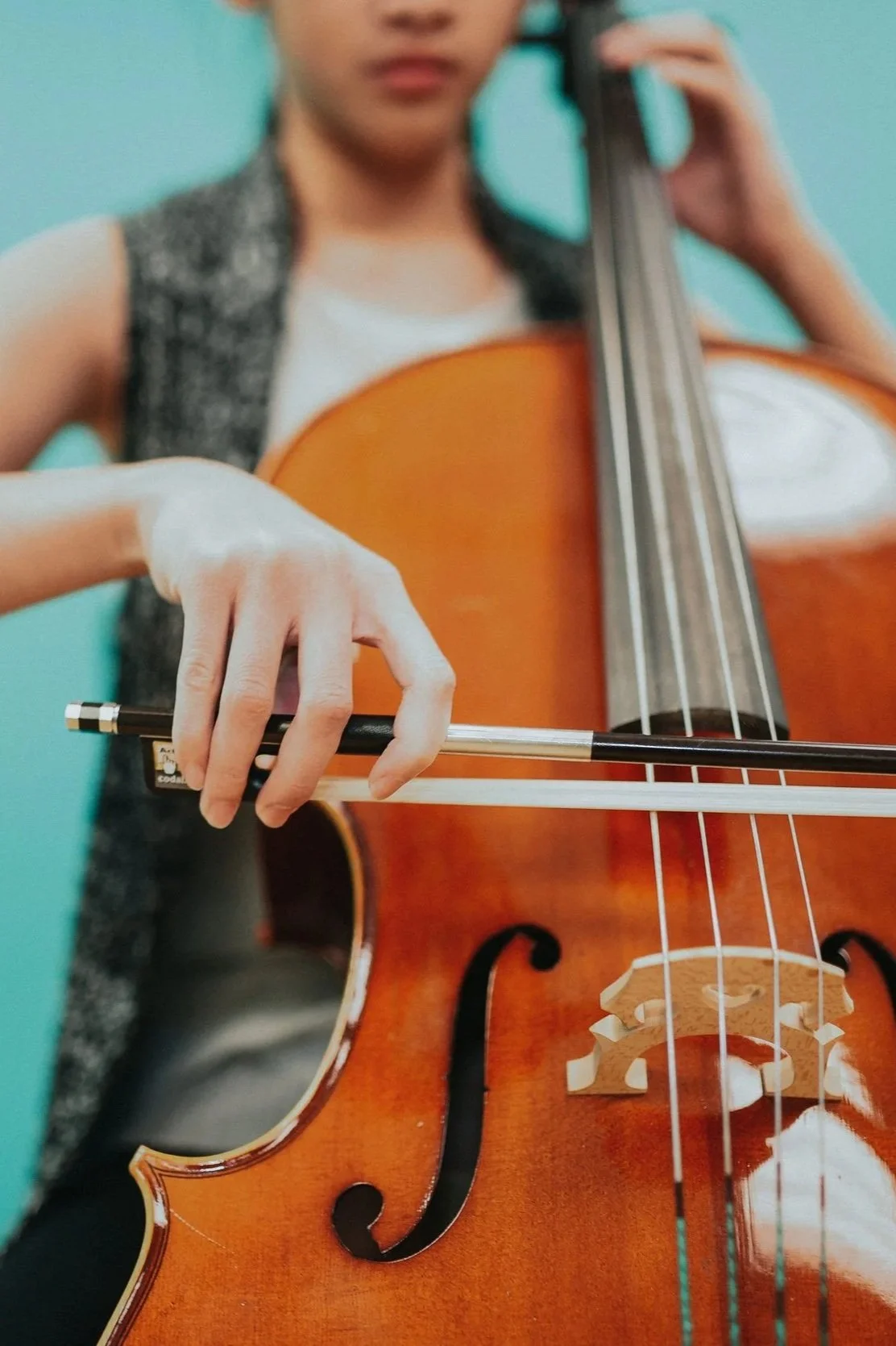 A person playing a cello, focusing on their hand holding the bow and the instrument.