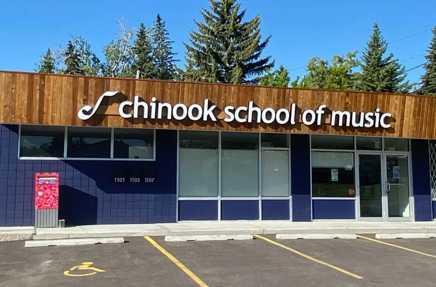 Front of a building with a wooden sign that reads 'Chinook School of Music' and a parking lot with designated handicapped parking spaces.