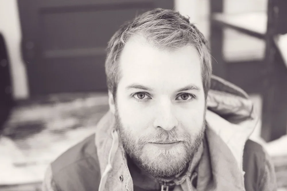 Close-up of a man with light hair, a beard, and mustache, looking at the camera with a neutral expression.
