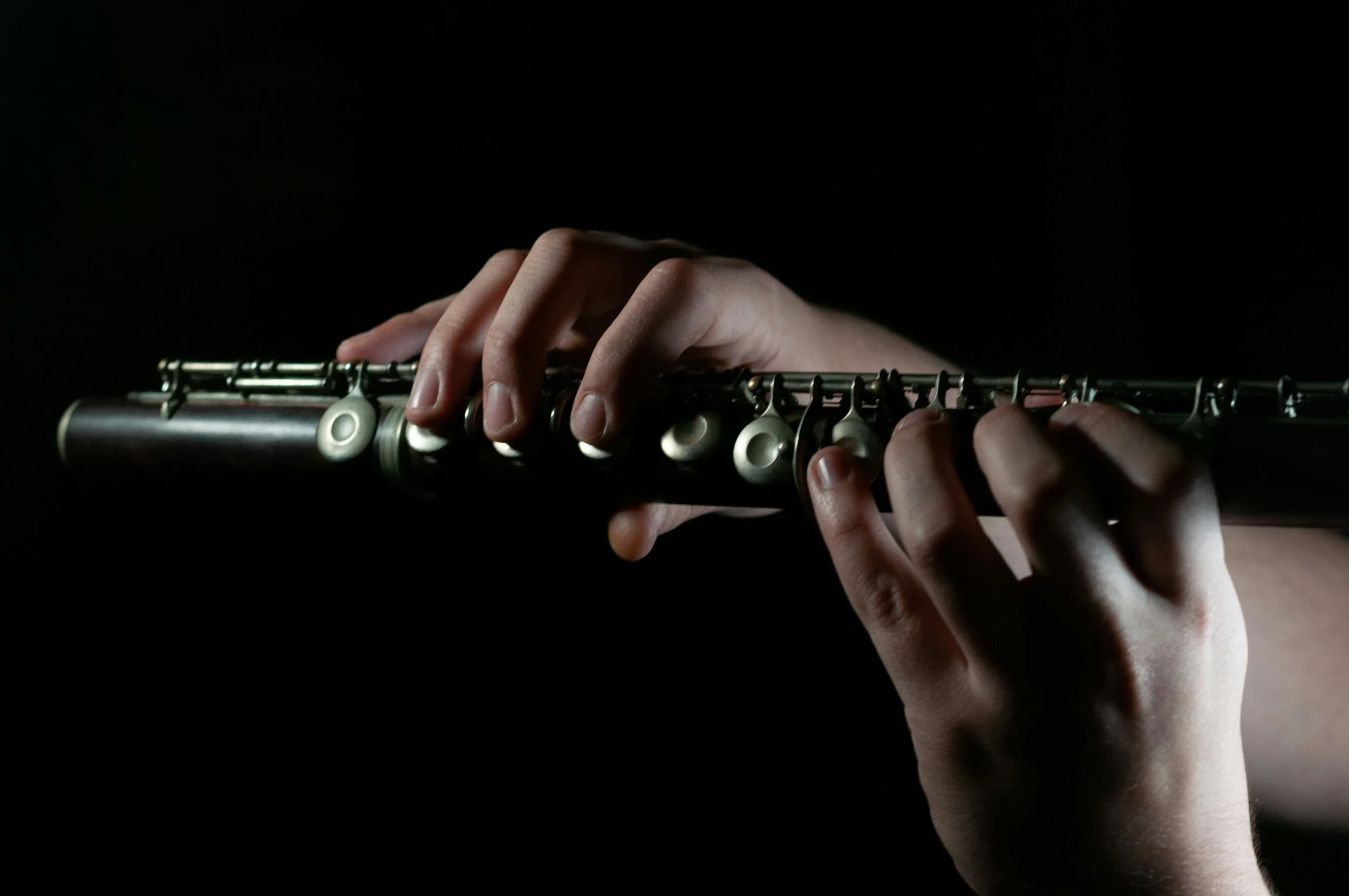 Close-up of hands playing a silver flute in a dark setting.
