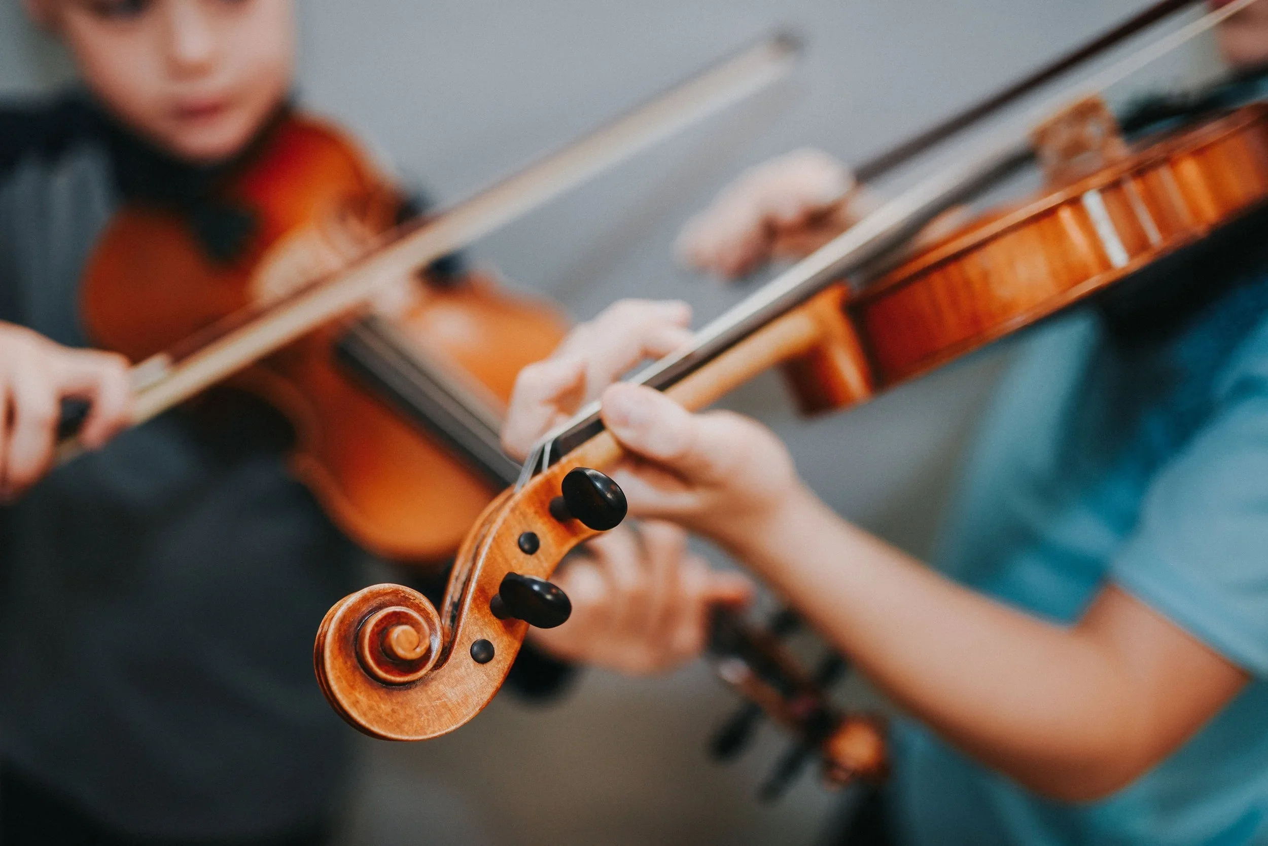 Close-up of two children playing violins, focusing on the scroll and hands of the instruments.