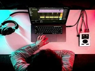 Person working on music production with laptop, headphones, and audio interface on a colorful desk.