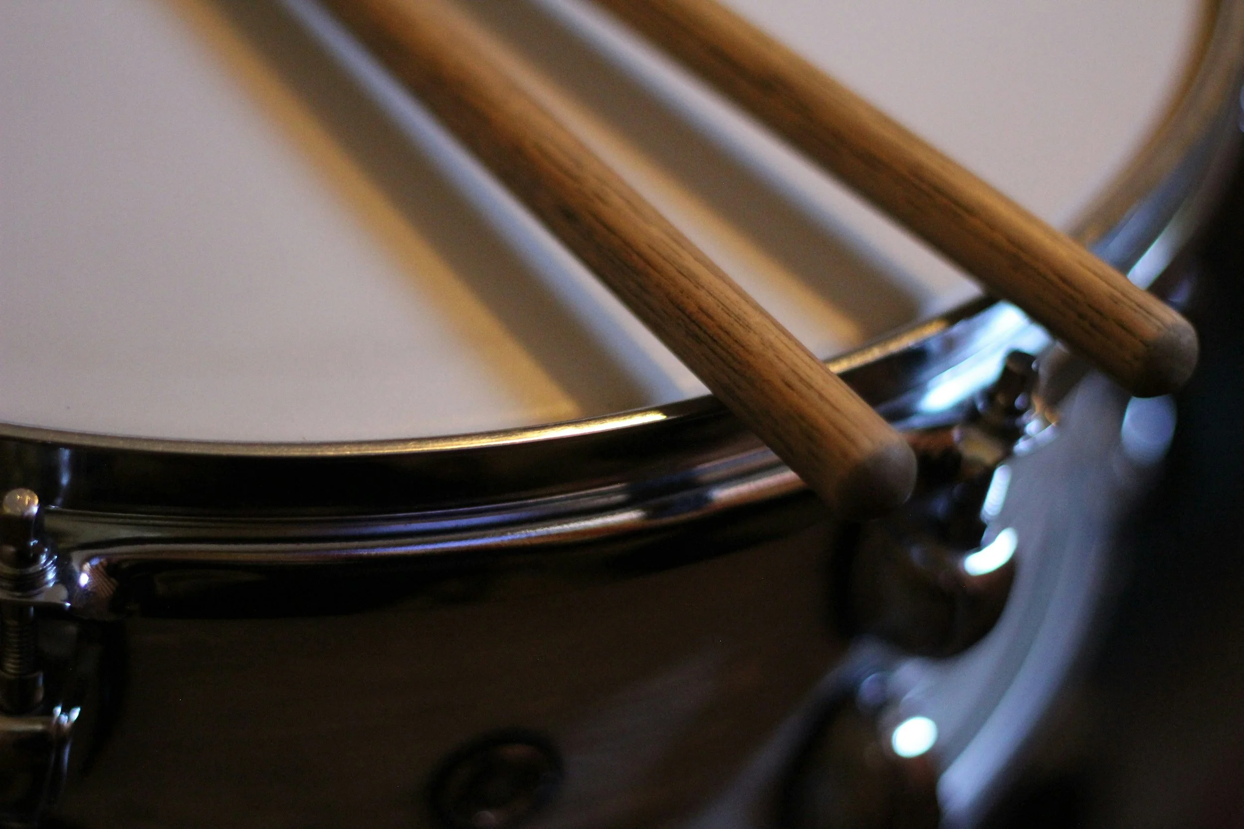 Close-up of a snare drum with two wooden drumsticks resting on top.