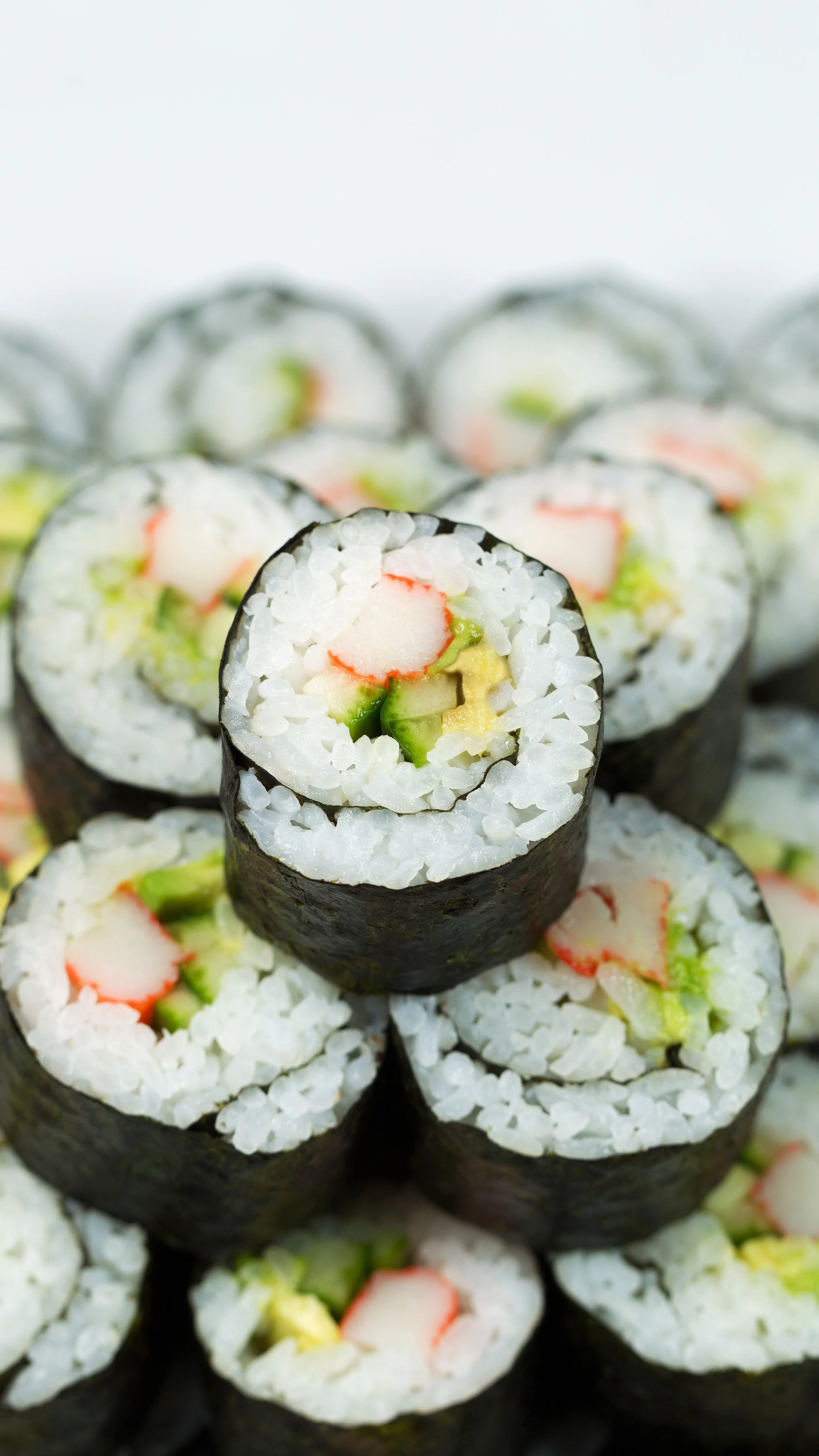 Close-up of sushi rolls filled with crab sticks, cucumber, and avocado, wrapped in seaweed.