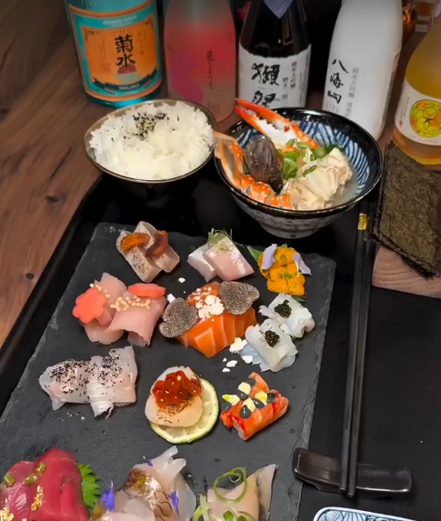 Assorted sushi with rice, and bowls of miso soup and beverages on a wooden table.