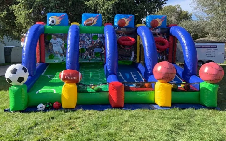 Inflatable sports-themed game with soccer, football, and basketball graphics, and large inflatable balls on the sides, set outdoors on grass.
