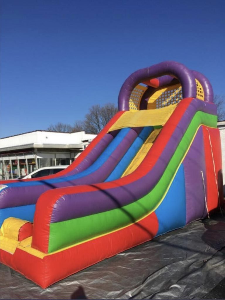 Colorful inflatable slide with purple, yellow, green, red, and blue sections outdoors on a sunny day.
