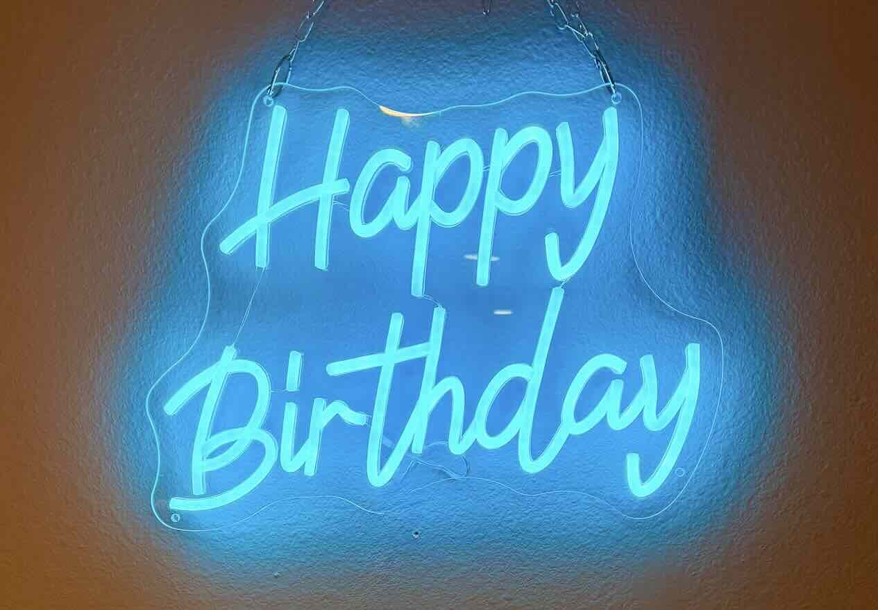 Blue neon sign that says "Happy Birthday" hanging on a wall.