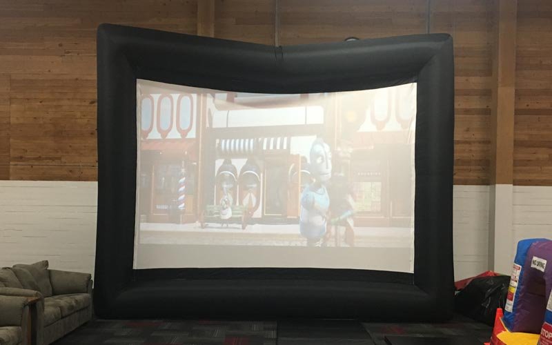 Indoor inflatable movie screen displaying a cartoon with characters, in a room with wooden walls and a couch to the left.