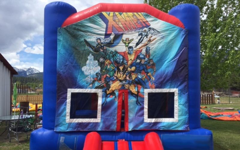 Colorful inflatable bounce house featuring Marvel's X-Men characters on the front, set outdoors on grass during daytime.