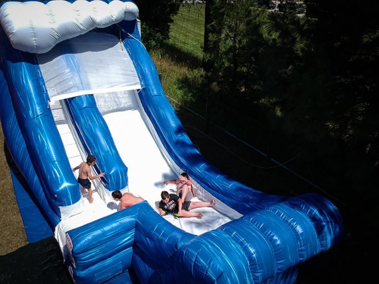 People sliding down an inflatable water slide outdoors during daytime.
