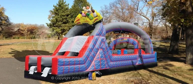 Colorful inflatable obstacle course with a dragon head at the entrance, set up outdoors on a grassy area with trees and a clear blue sky in the background.