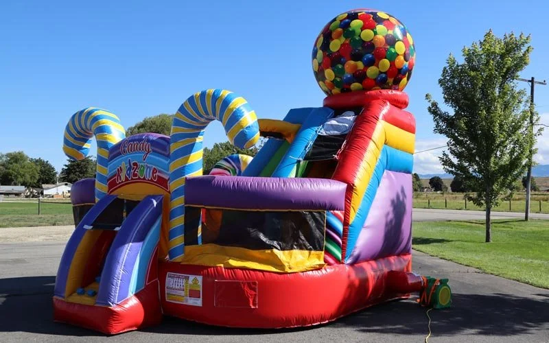 Colorful inflatable bounce house shaped like a candy machine with a gumball sphere on top, located outdoors on a sunny day.