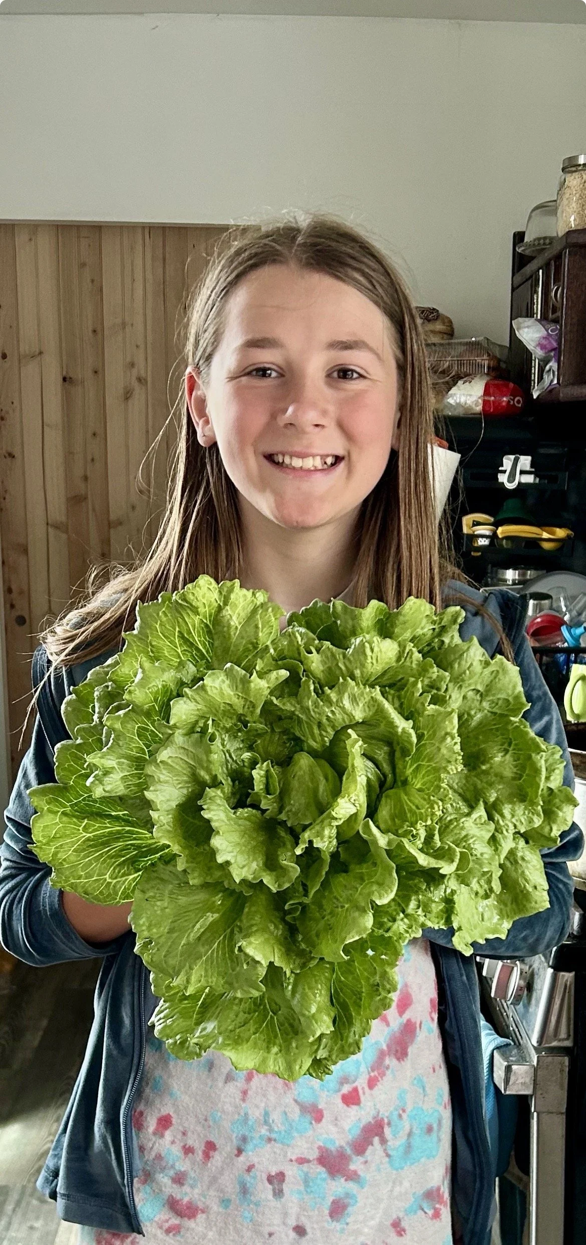 Luka Doherty founder of Cooler Crops with long brown hair, smiling and holding a large head of green lettuce indoors.