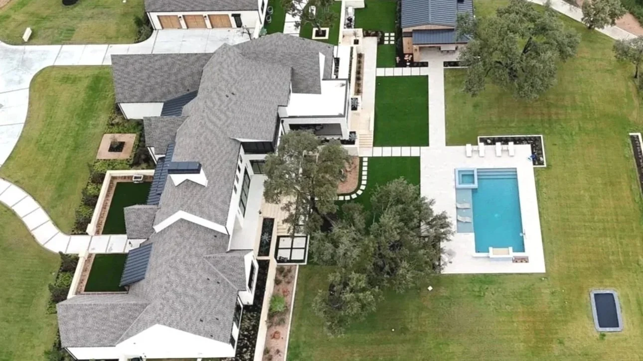 Aerial view of a modern house with a large backyard, swimming pool with lounge chairs, and landscaped lawns and trees.
