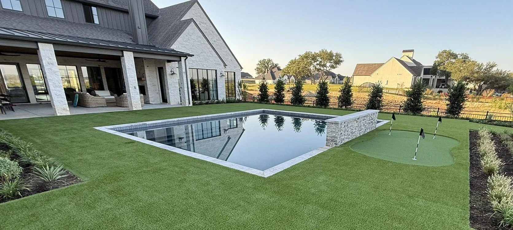 Backyard with a custom swimming pool, putting green, and well-maintained lawn outside a modern house with large windows and an outdoor seating area. Best of hood county. dfw pools