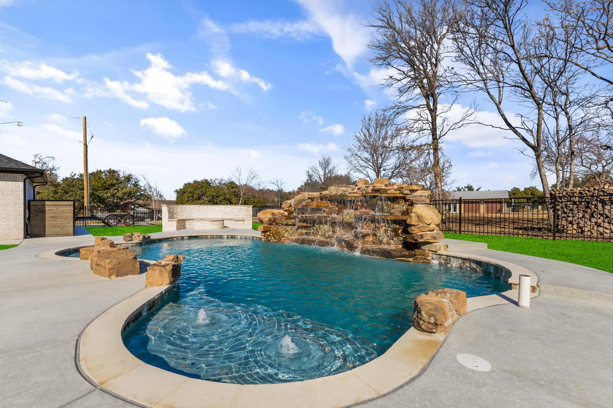 A backyard with a swimming pool featuring a rock waterfall and fountain. texas. best of hood county. family owned. quality. luxury. ultimate custom pools. fort worth. texas. honest. trusted. great reviews. Best in texas. top pool company. water