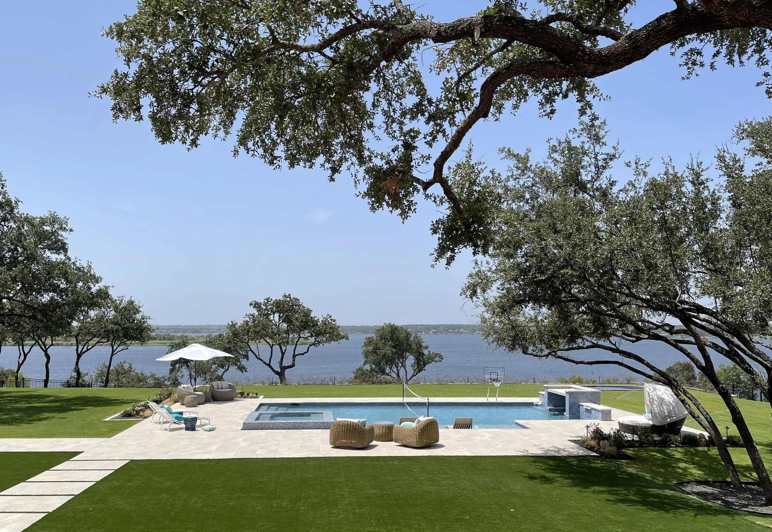 Backyard with swimming pool overlooking a body of water, trees, and a clear sky.
