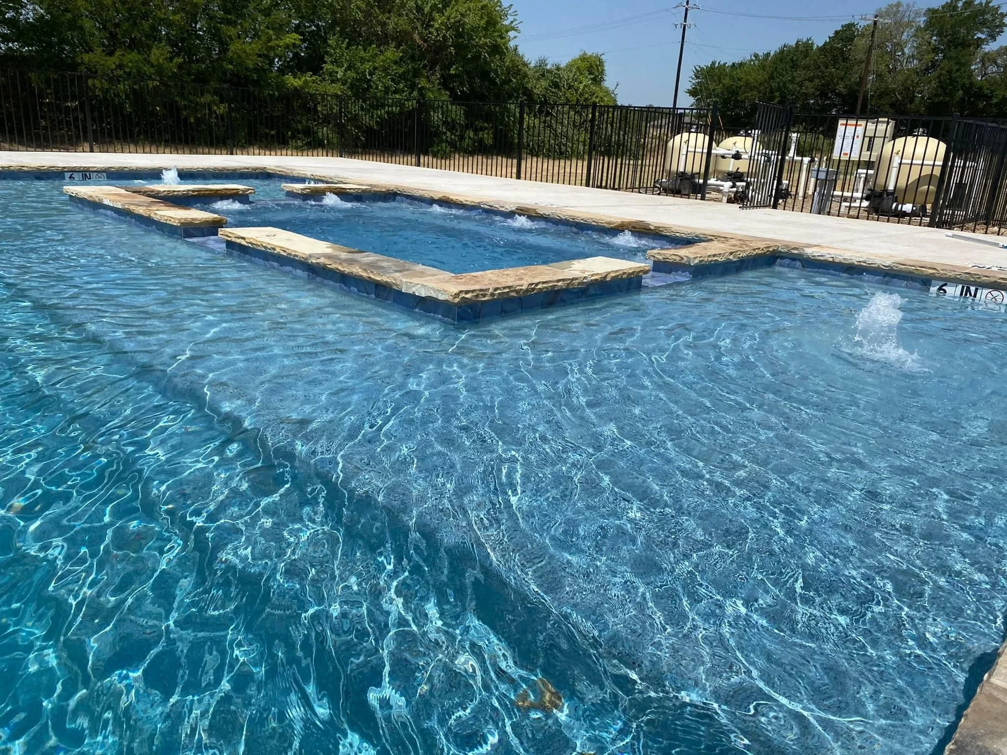 custom swimming pool with a shallow section and a deep section, surrounded by a black metal fence. back yard design. texas. best of hood county. family owned. quality. luxury. ultimate custom pools. fort worth. honest. trusted. great reviews. Builder