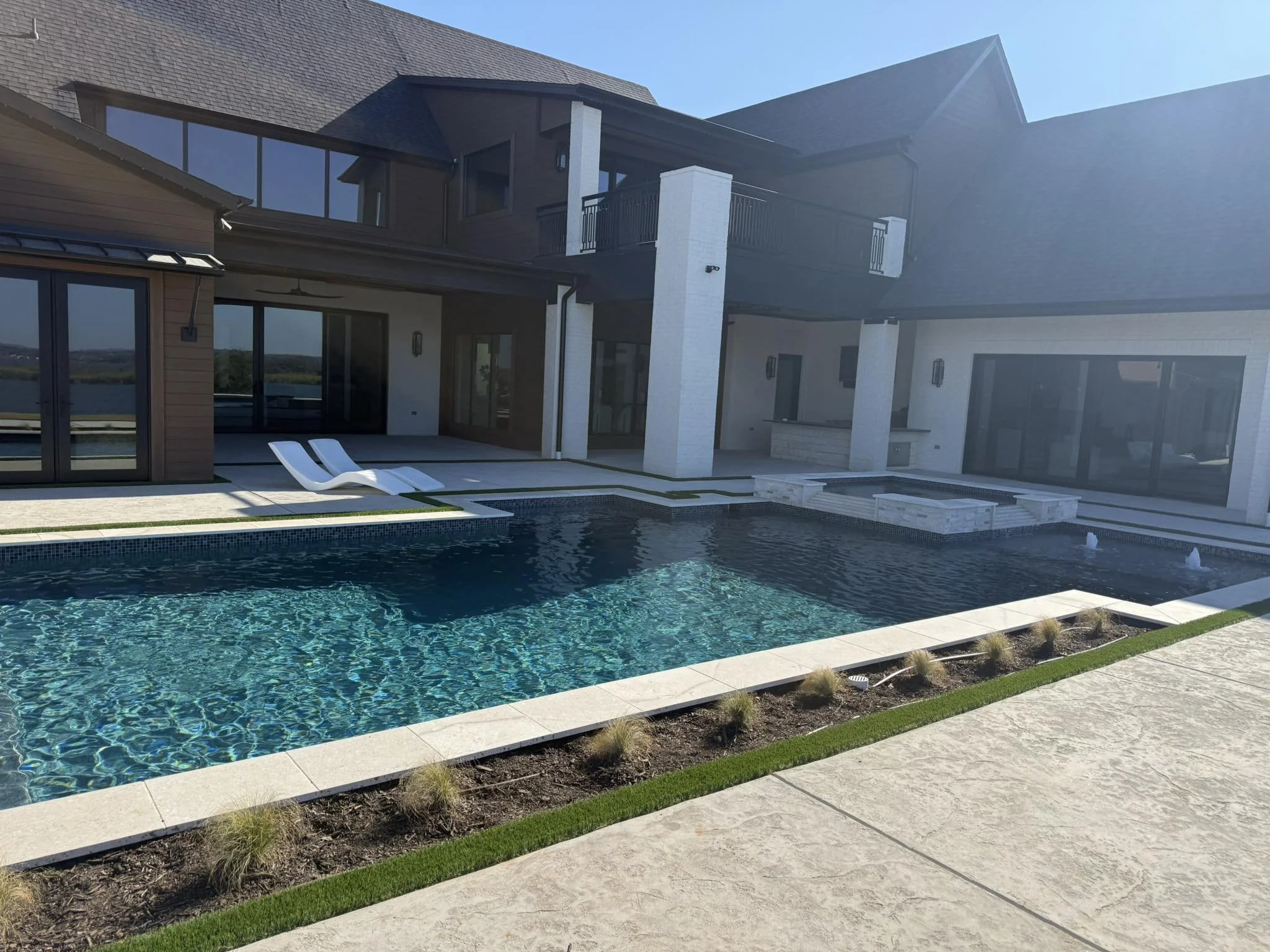 Modern house with a swimming pool in the backyard, featuring lounge chairs, a water fountain, and outdoor amenities, under clear blue skies.