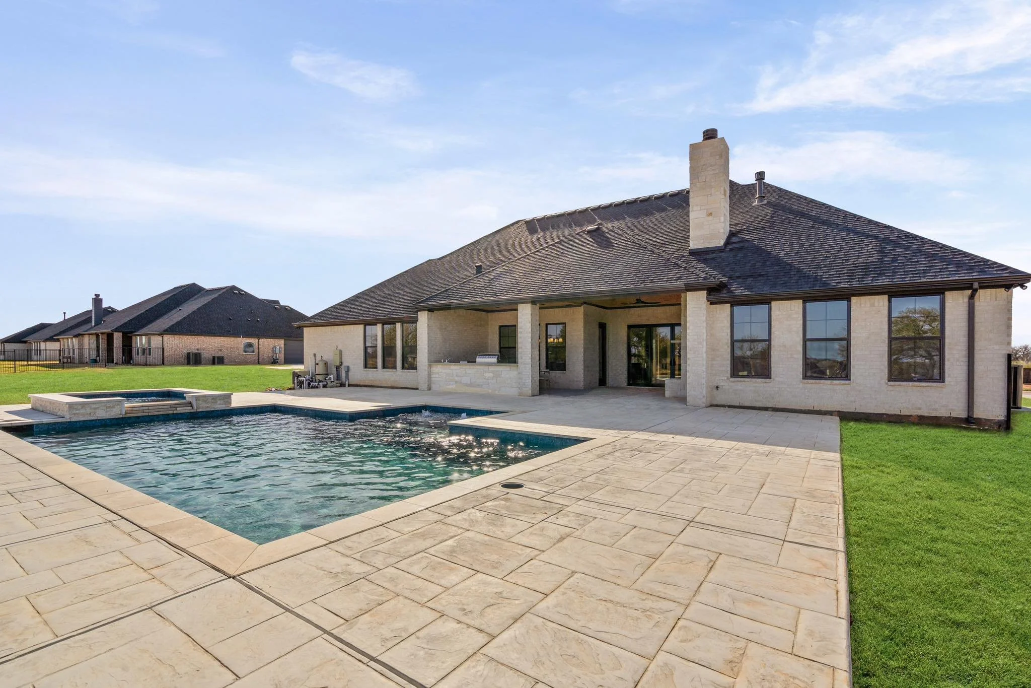 Backyard of a house with a swimming pool, patio area, and well-maintained lawn under a clear blue sky. custom pool design. trusted builder. granbury. texas fort worth. cleburne. best of hood county. dfw pools.