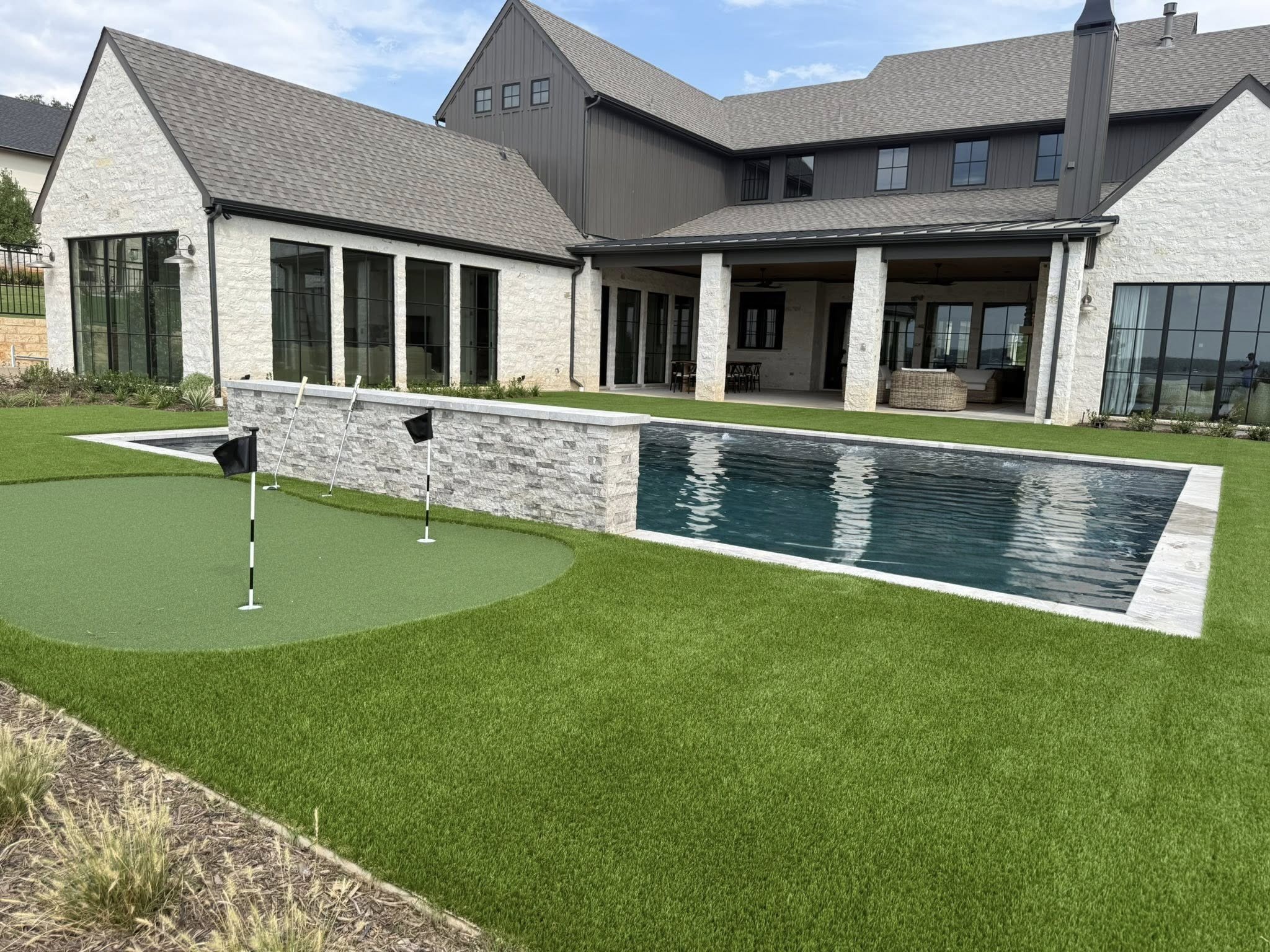 Luxury house with a backyard featuring a swimming pool, putting green, and outdoor patio furniture.