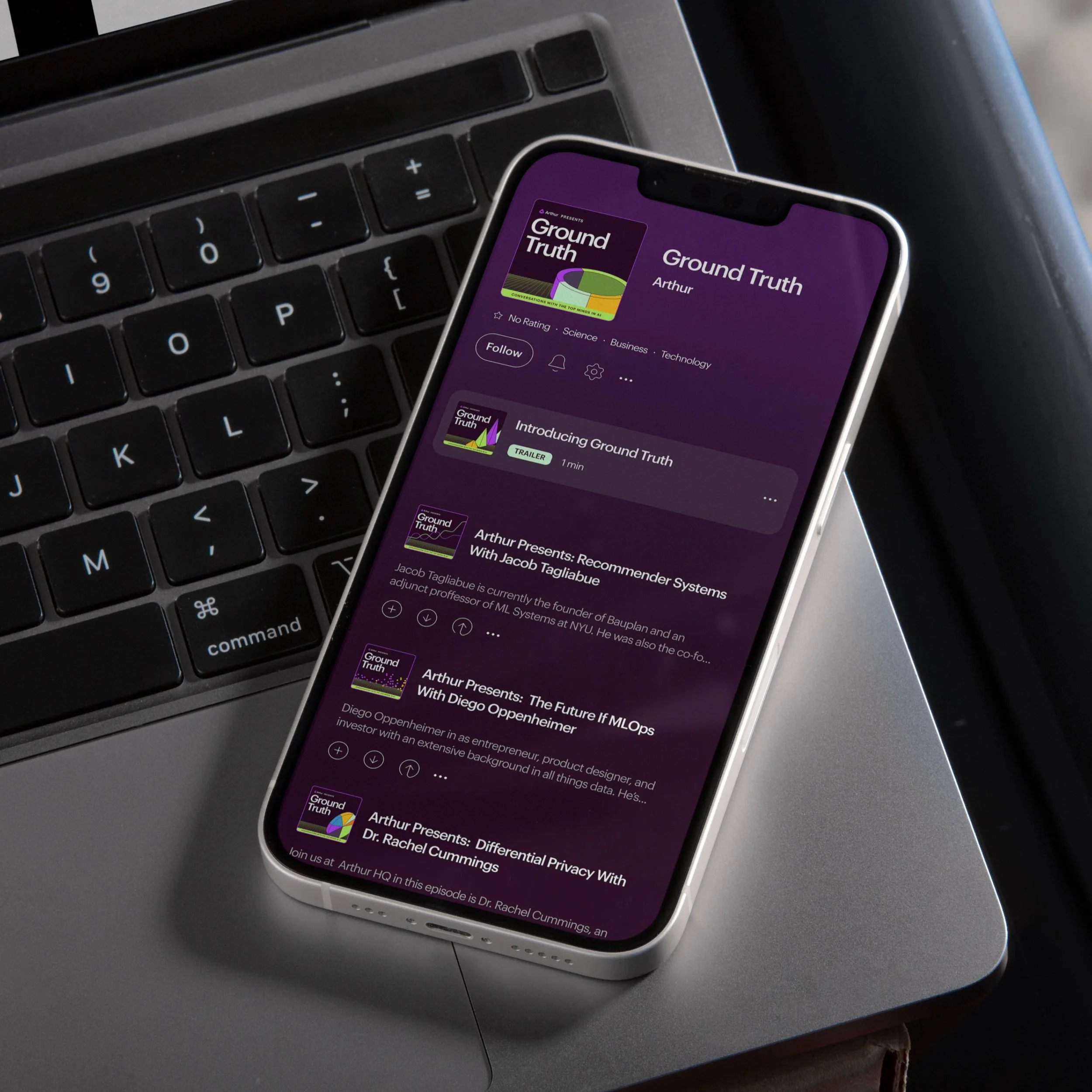 Close-up of a thinkpad laptop with a smartphone resting on it, displaying a podcast app featuring the episode titled 'Ground Truth' with a purple and green cover art on the phone screen.