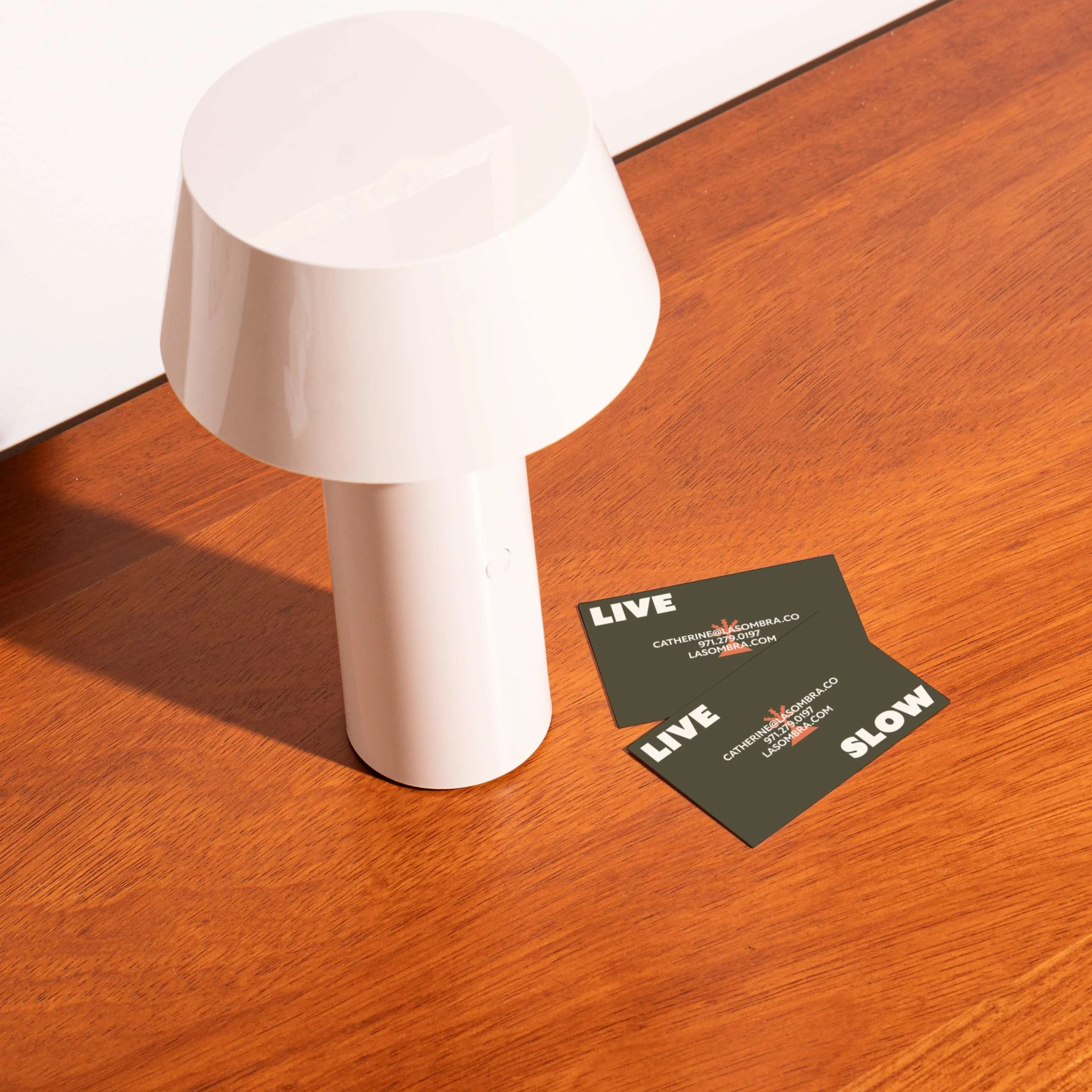 A white cylindrical object on a brown wooden surface with a black card reading 'LIVE SLOW' and contact information.