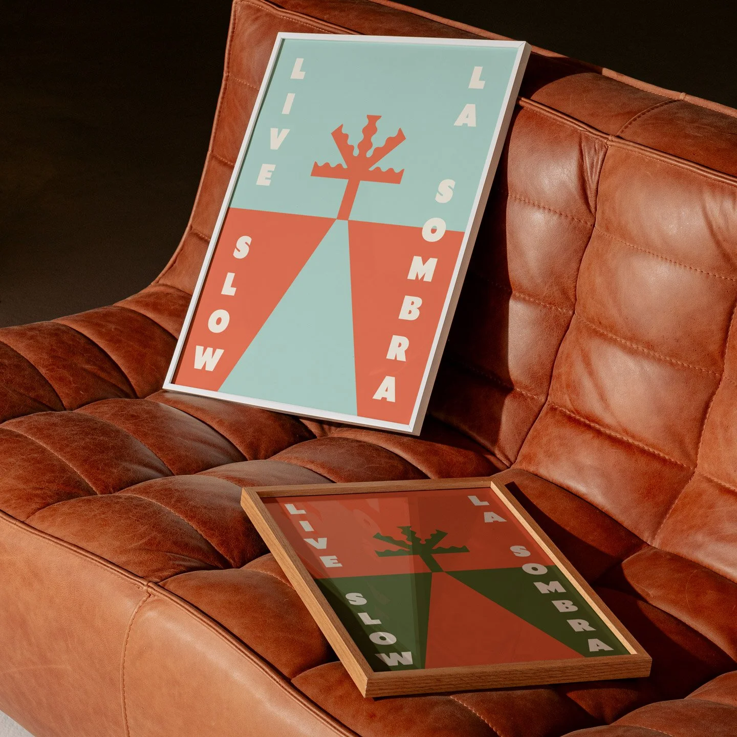 Two Christmas-themed signs with words and a stylized Christmas tree graphic on a leather couch. One sign is upright and the other is face down on the couch.