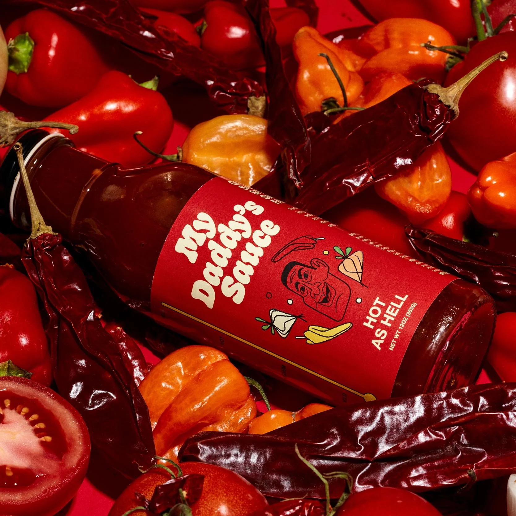 Close-up of a bottle of hot sauce surrounded by red and orange peppers on a red background.