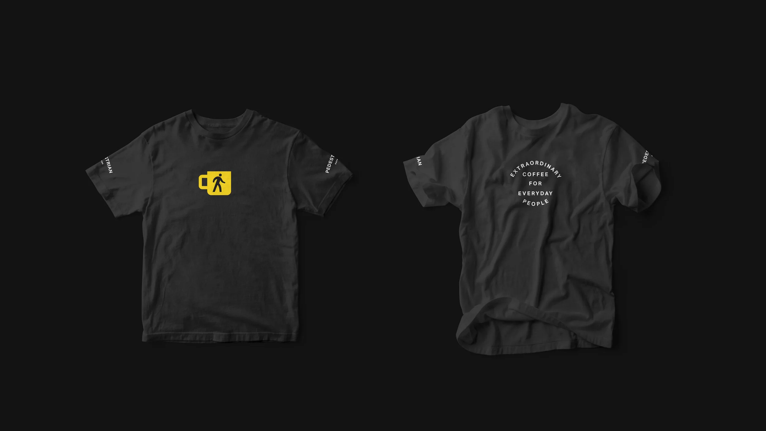 Two black T-shirts on a dark background; the left T-shirt has a yellow coffee cup icon with a walking person, and the right T-shirt has white text that reads 'Extraordinary Coffee for Everyday People' with additional text along the sleeves.