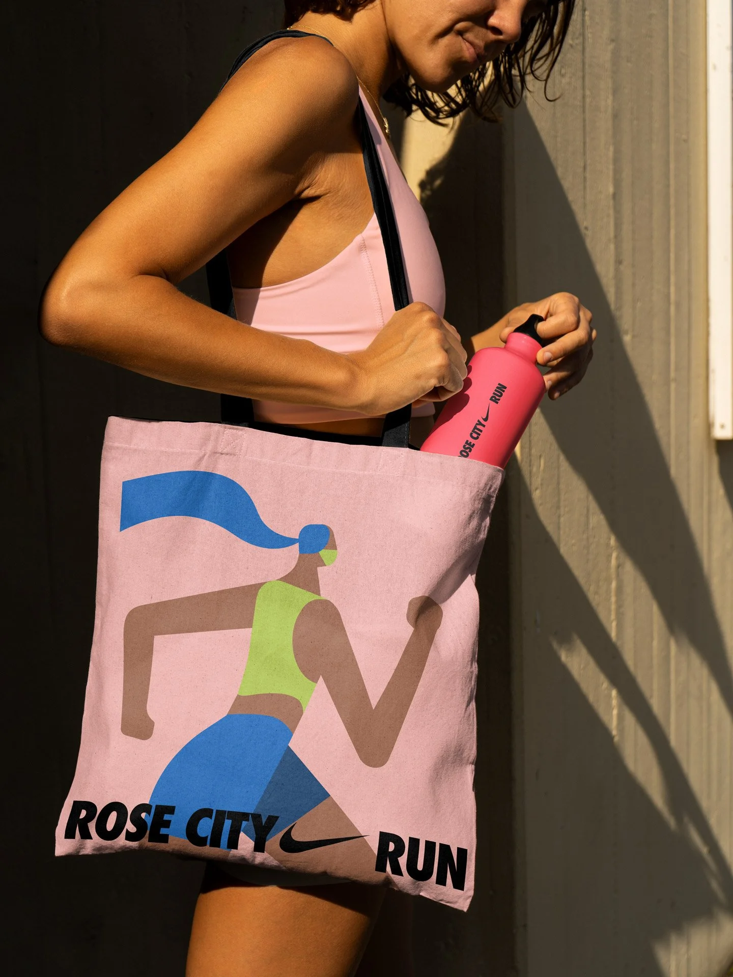 A woman in workout attire holding a pink water bottle and a sports bag with a running graphic and the words 'Rose City Run' and the Nike logo.